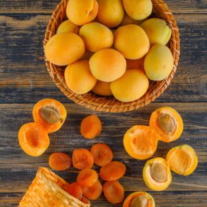 Apricots with dried apricots in a wicker basket on wooden background, top view.